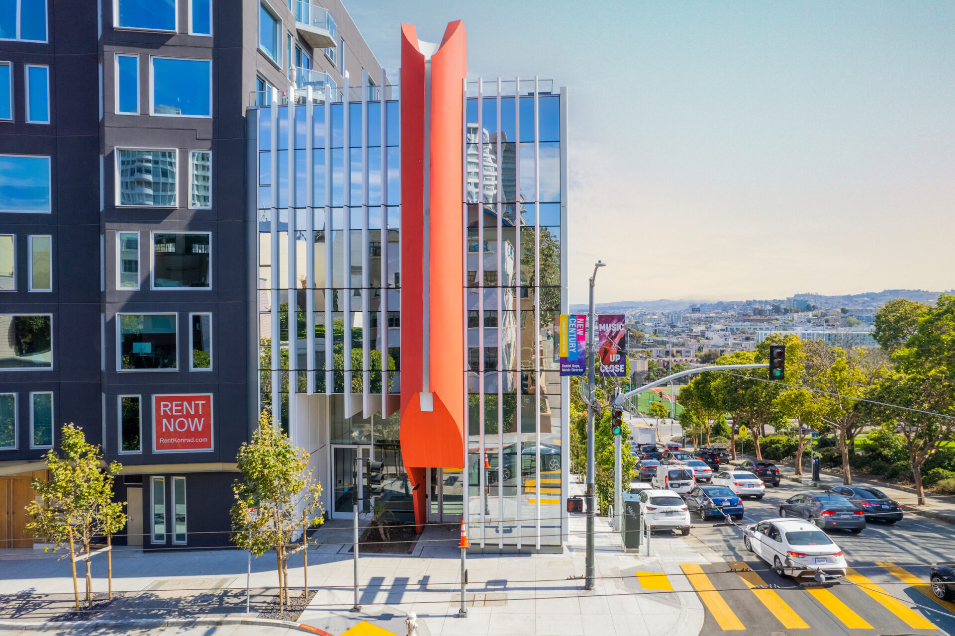 Modern urban building located on a busy city street with cars and greenery in the background.